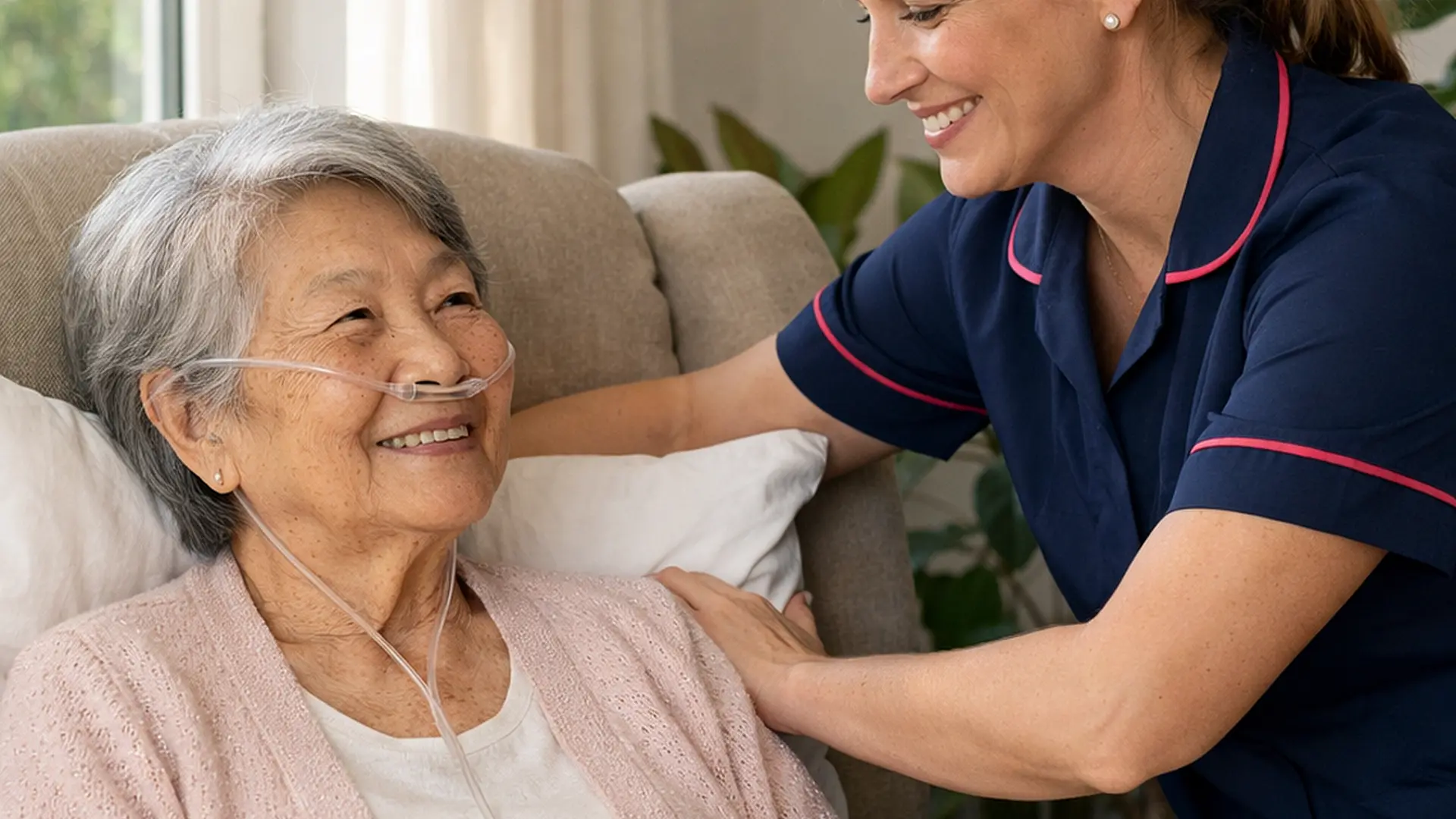 Realistic scene of a white female caregiver in a 00072b tunic with e51974 piping gently adjusting cushions for an elderly Asian woman seated in a reclining chair oxygen tubing visible sun streaming through window houseplants nearby both sharing a soft smile showing comfort and understanding.