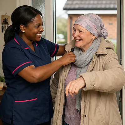 Warm realistic scene of a black female caregiver in a 00072b tunic with e51974 piping helping a white woman with a headscarf put on a coat near the front door both chatting and smiling before a hospital appointment.